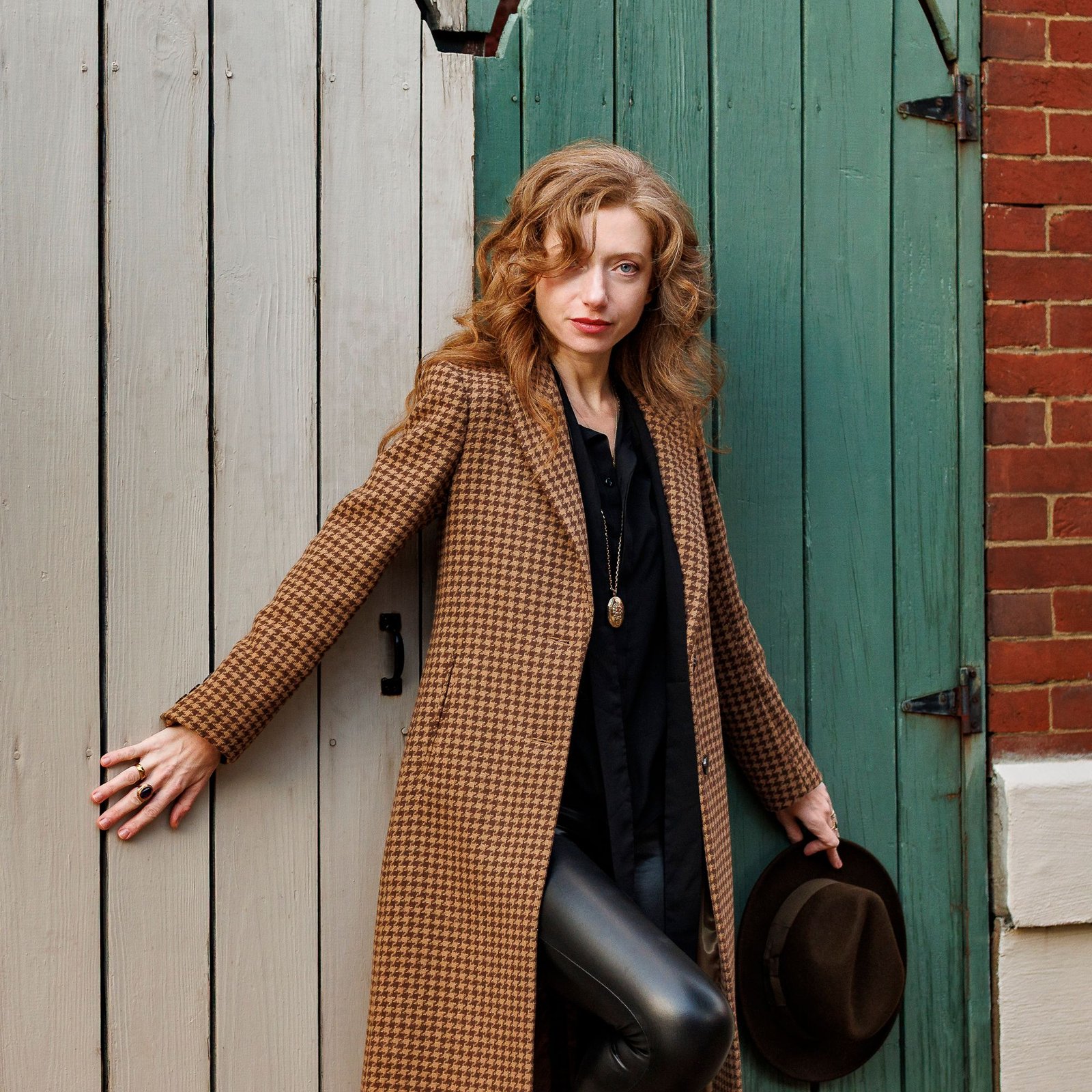 Olya in a houndstooth coat, leaning against a weathered green wooden door
